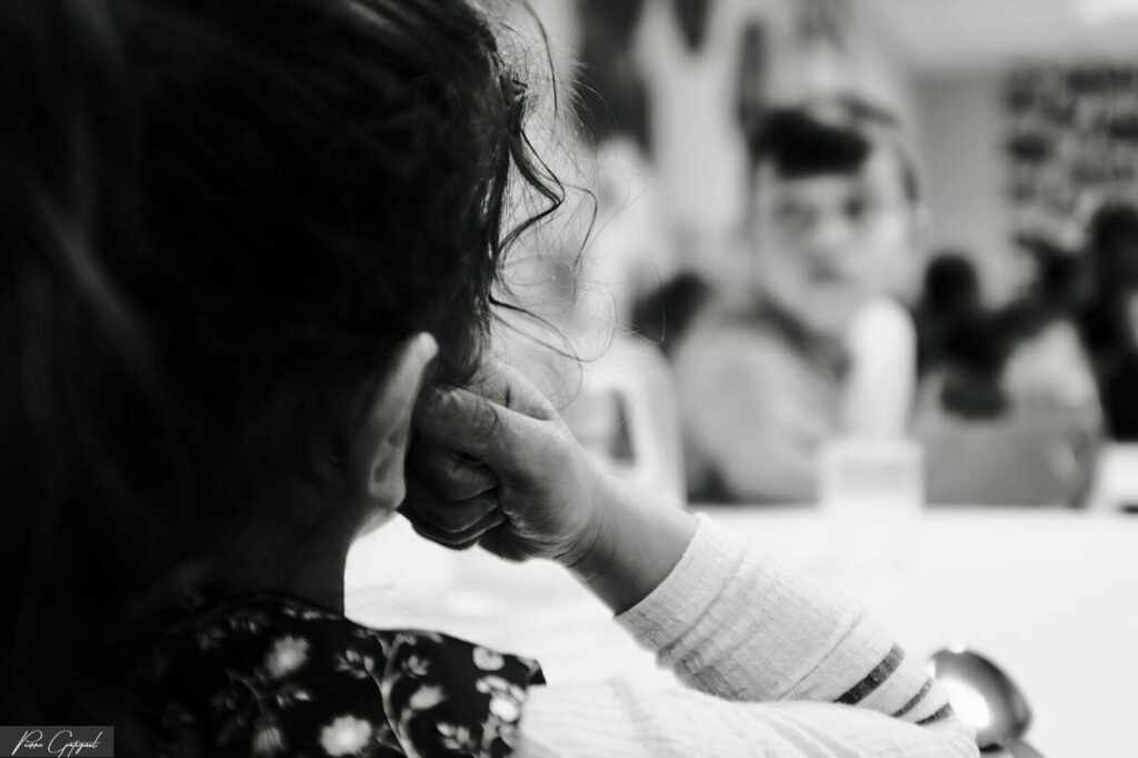Child seen from behind, hand to face, blurred people in the background